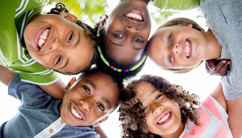 Diverse group of smiling kids with arms around each other looking down into camera