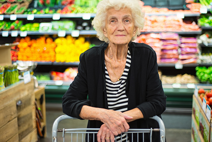 Elderly woman with shopping cart smiling at camera inside grocery store