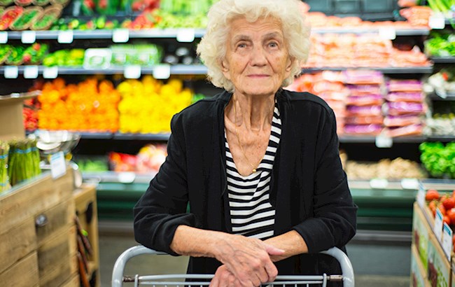 Elderly woman with shopping cart smiling at camera inside grocery store