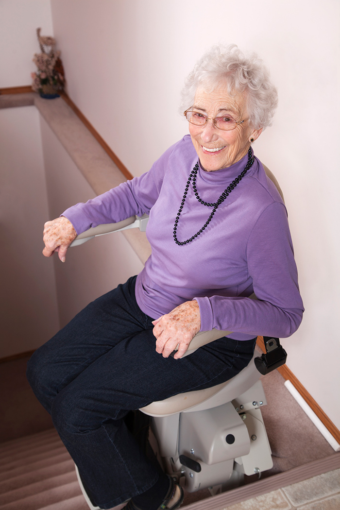 Elderly woman using lift chair to move her upstairs in home