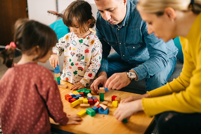 Parents and two small kids sitting around coffee table playing with building blocks