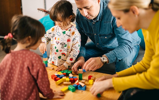 Parents and two small kids sitting around coffee table playing with building blocks