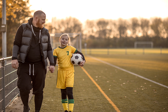 Father walking with daughter outside wearing soccer uniform and holding soccer ball