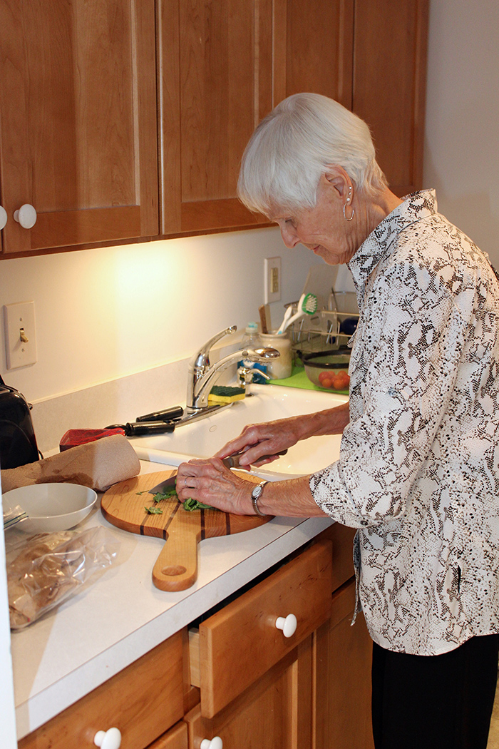 Senior woman in kitchen standing cutting vegetables on cutting board