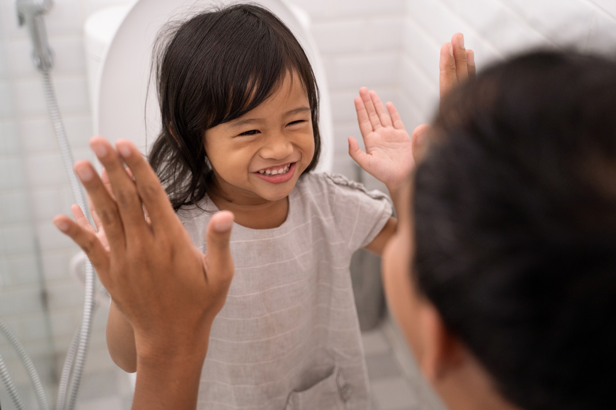 Toddler sits on toilet for potty training and gives adult a high five.