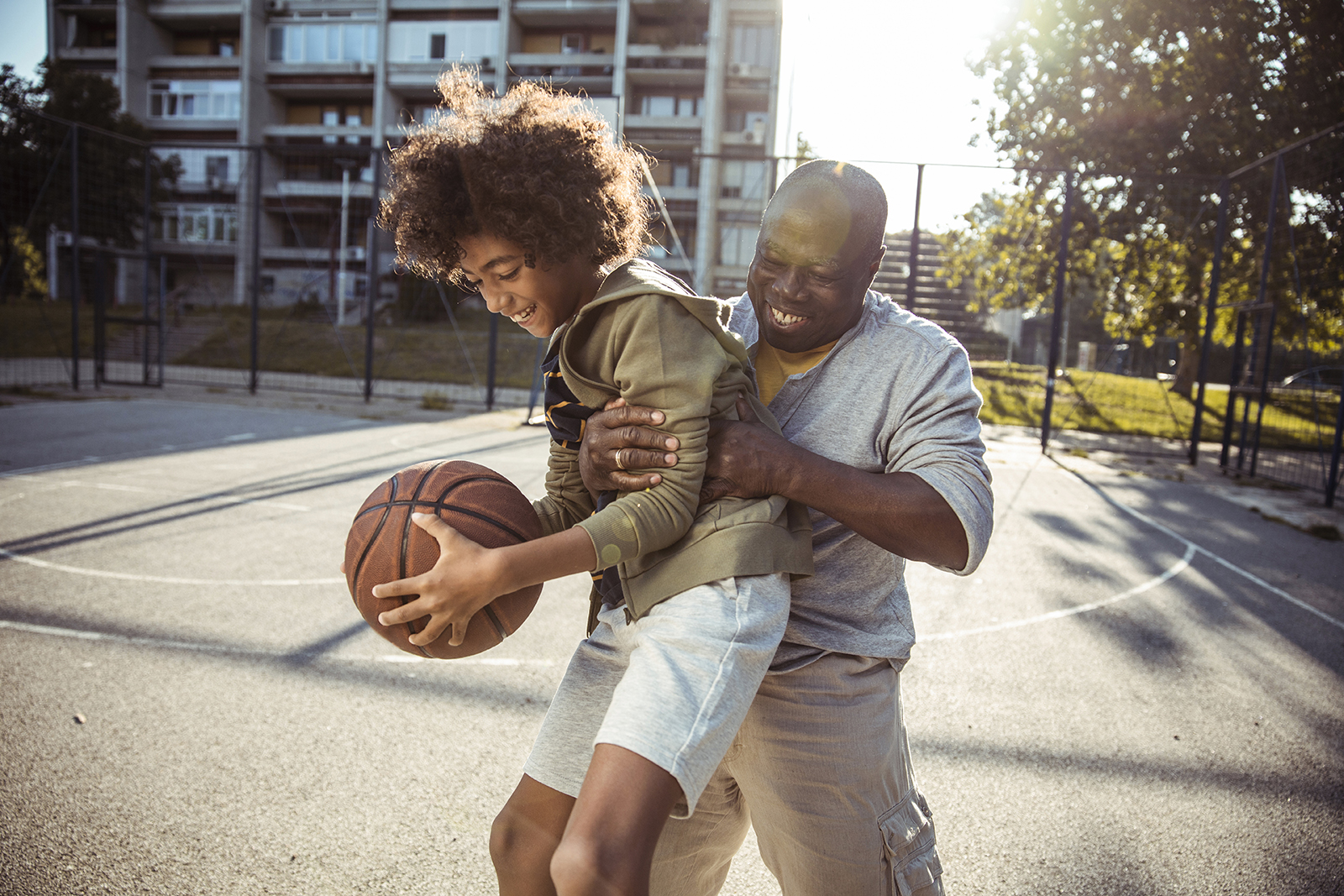 Man playing basketball outside with young kid