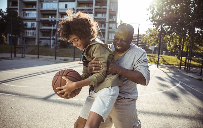 Man playing basketball outside with young kid