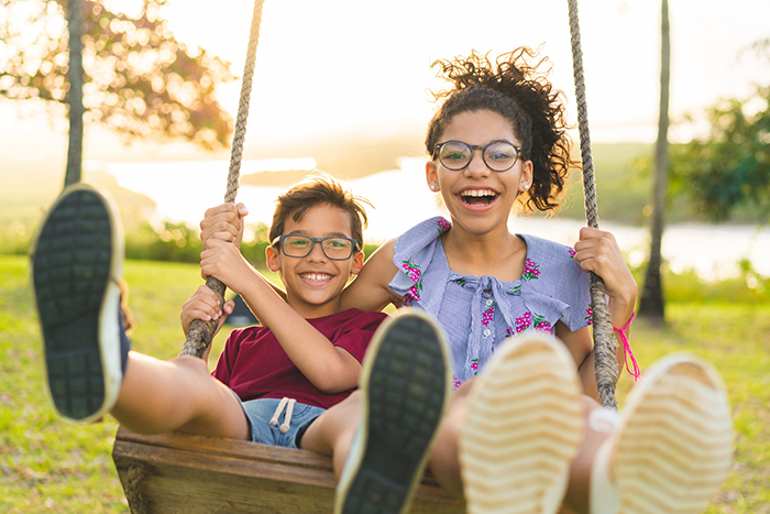 Smiling young boy and girl outside on wood swing with lake in background