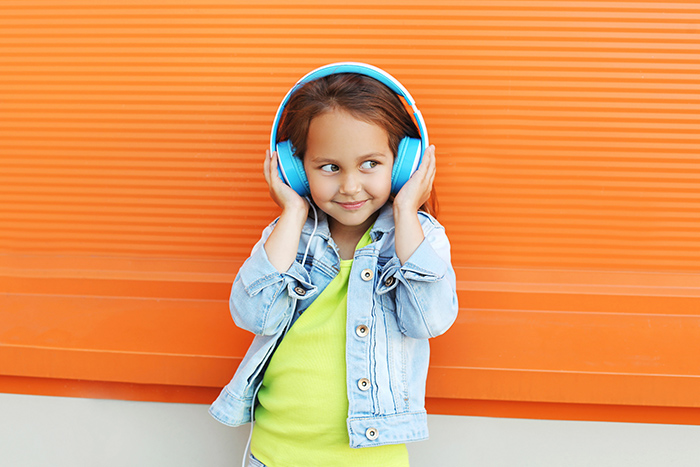 Young girl smiling waring teal headphones in front of orange wall