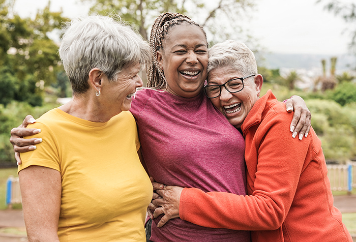 Three older women with arms around each other laughing outside