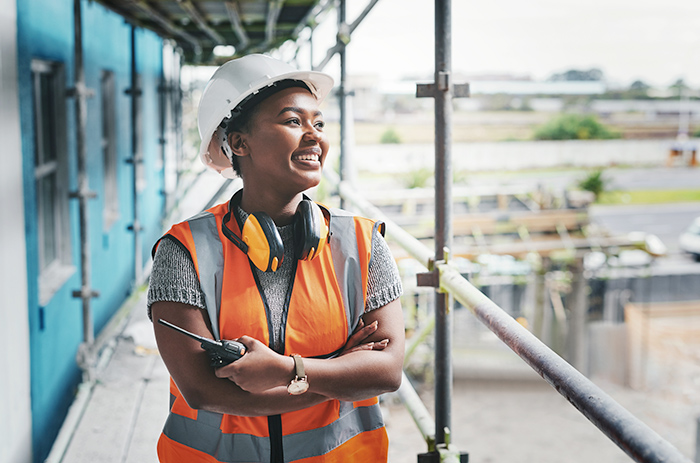Woman wearing orange reflective vest and hardhat smiling at construction site