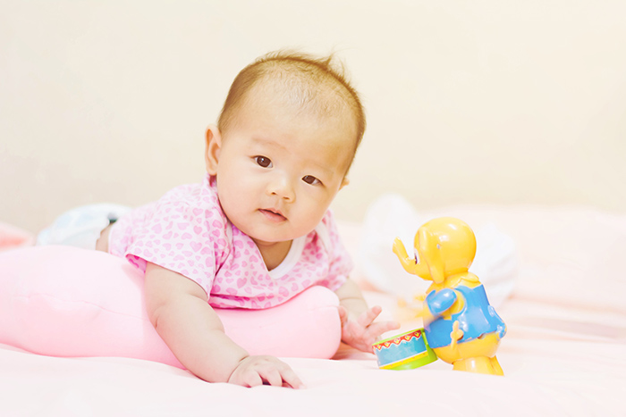 Infant laying on pillow practicing tummy time with elephant toy