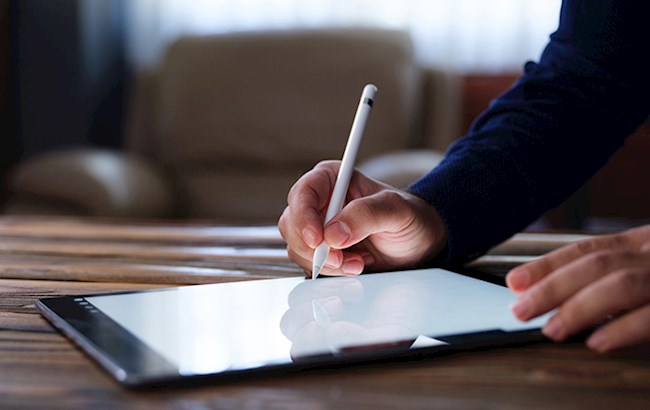 Male hands holding stylus pen writing on tablet on desk