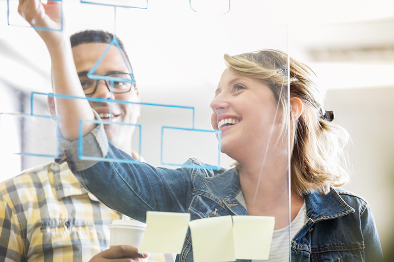 Man and woman behind glass wall drawing flow chart with blue marker