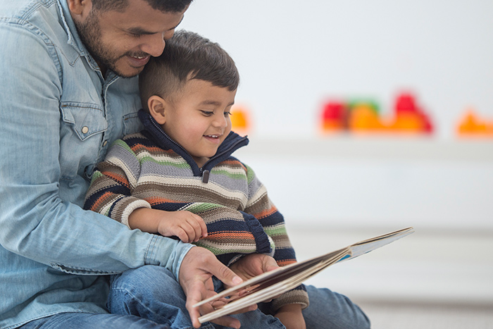 Smiling toddler sitting in mans lap reading a book