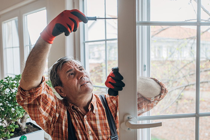 Older man wearing gloves holding a screw driver fixing door