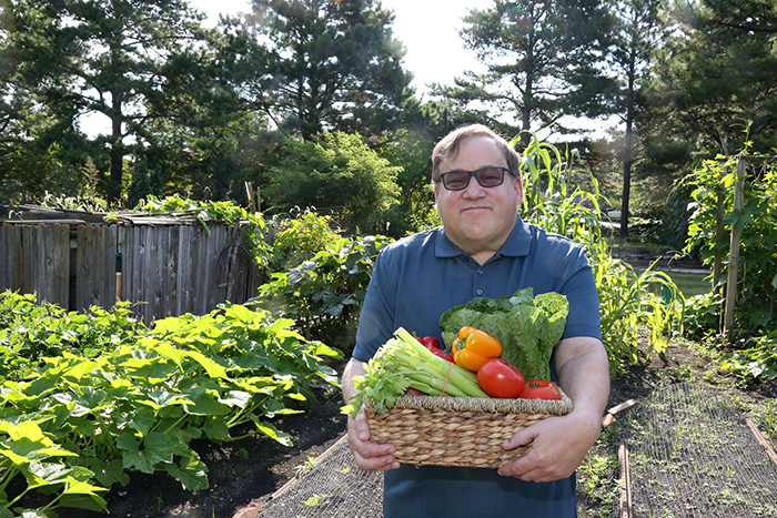 Man outside in garden holding basket of fresh vegetables