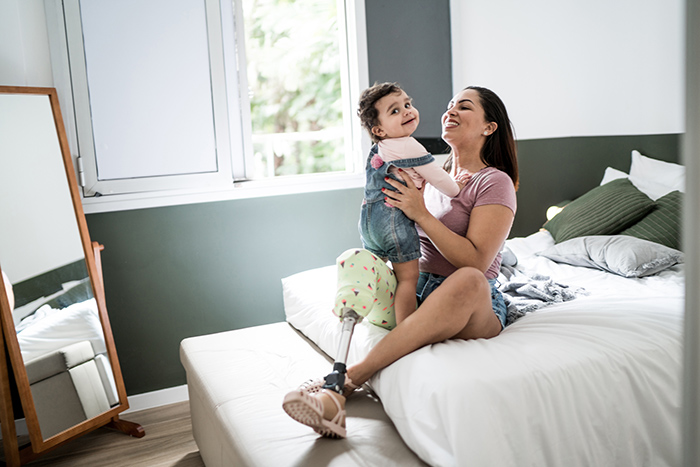 Woman sitting on bed with prosthetic leg holding up smiling toddler