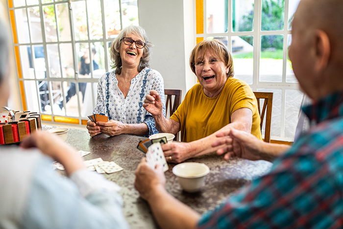 Two senior women and a man playing cards at a table laughing