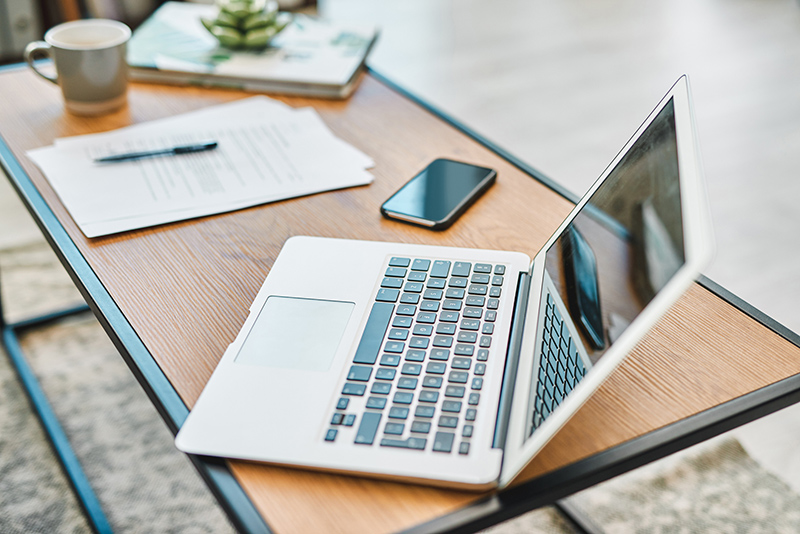 Open laptop on top of desk alongside cell phone and paperwork