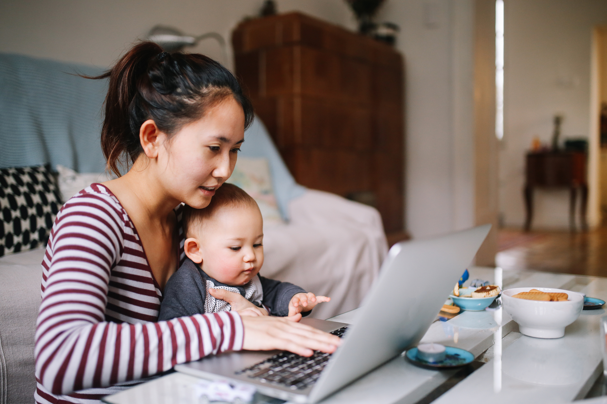 Parent sitting at a table with baby looking at a laptop
