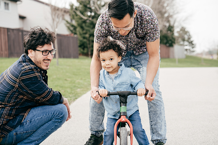 Two men helping small child ride a bike outside