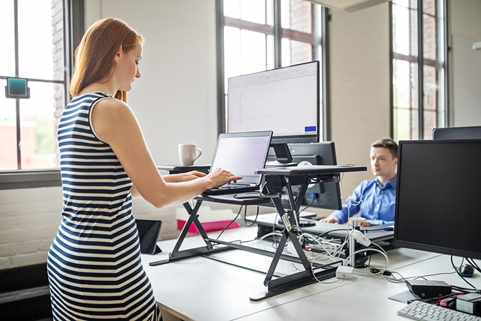 Professional woman typing on laptop using a standing desk in office