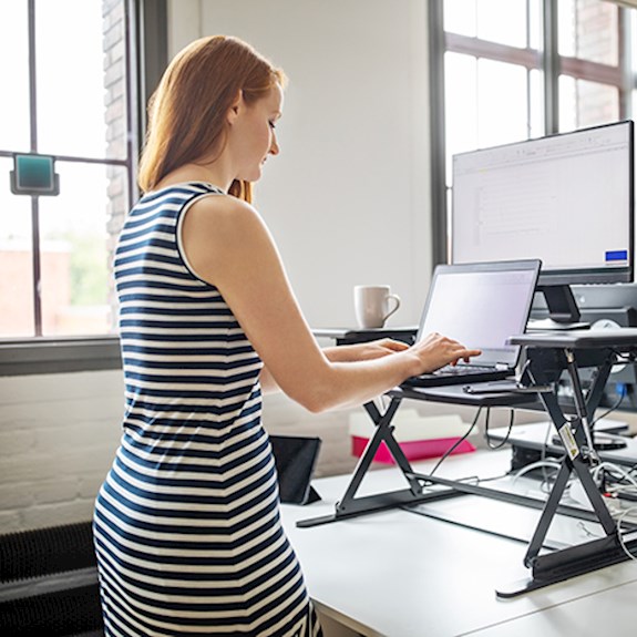 Professional woman typing on laptop using a standing desk in office