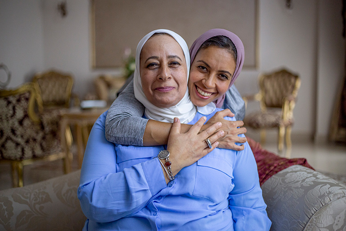 Smiling older and younger woman wearing head scarves embracing inside house