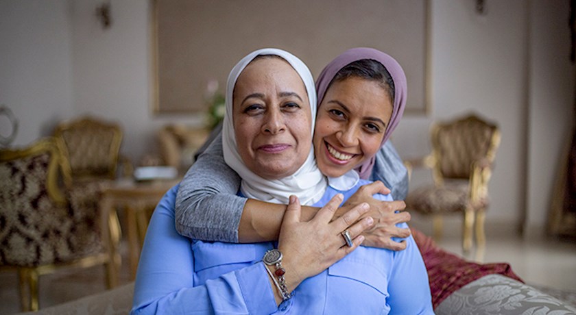 Smiling older and younger woman wearing head scarves embracing inside house