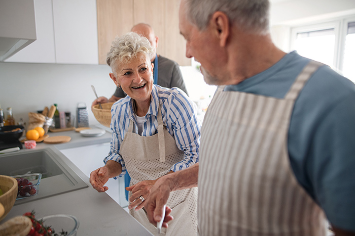 smiling senior woman and man with aprons in kitchen cooking