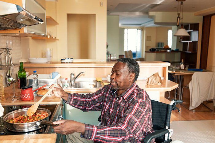 Man sitting in wheelchair cooking at stove inside kitchen