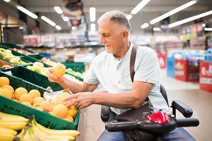 Man in motorized wheelchair at grocery store looking at oranges