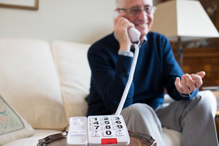 Close up of telephone with extra large buttons and man talking on receiver in background