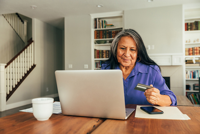 Senior woman sitting at laptop with credit card in her hand 