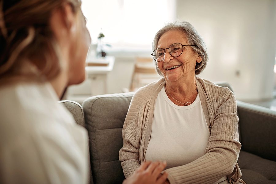 Smiling senior woman talking to another person on a couch in Skilled Nursing Facility