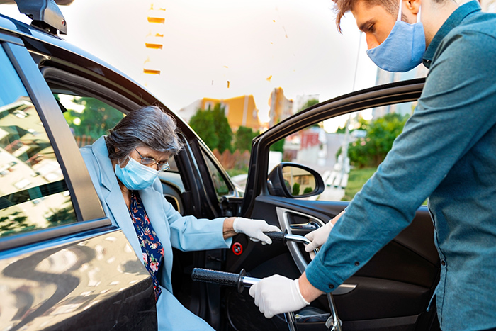 Young man wearing face mask helping older woman with face mask get out of car with a walker