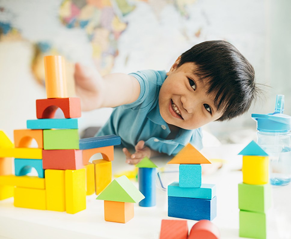 Smiling young boy laying on the floor playing with building blocks