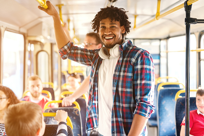 Smiling man wearing headphones around neck standing on public bus holding handrail