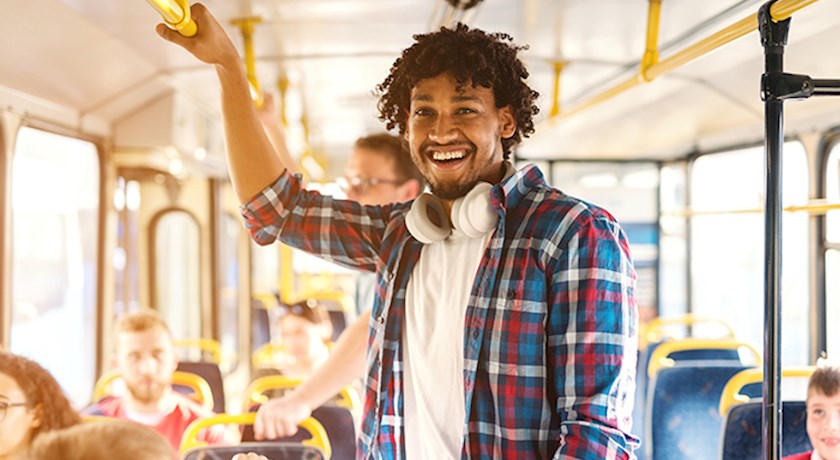 Smiling man wearing headphones around neck standing on public bus holding handrail