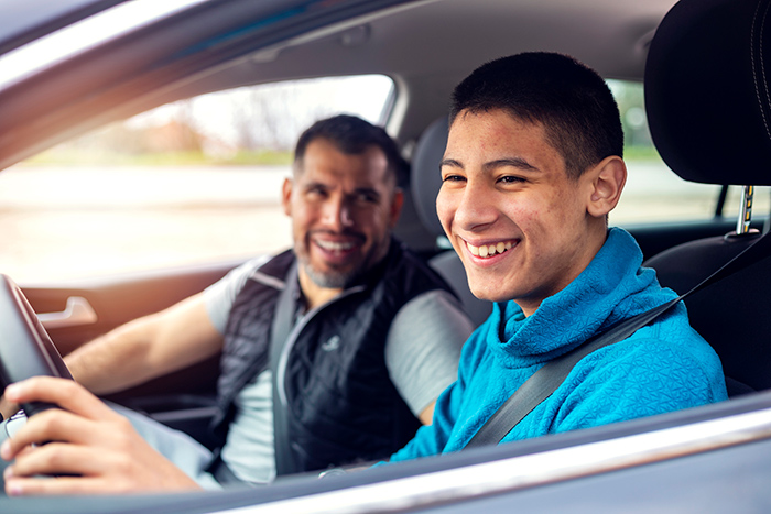 Older man in car with smiling teenage boy behind the steering wheel driving