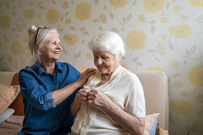 Senior woman sitting on couch helping elderly woman put on sweater