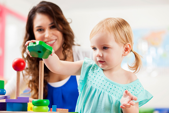 Toddler girl playing with blocks with female smiling in background