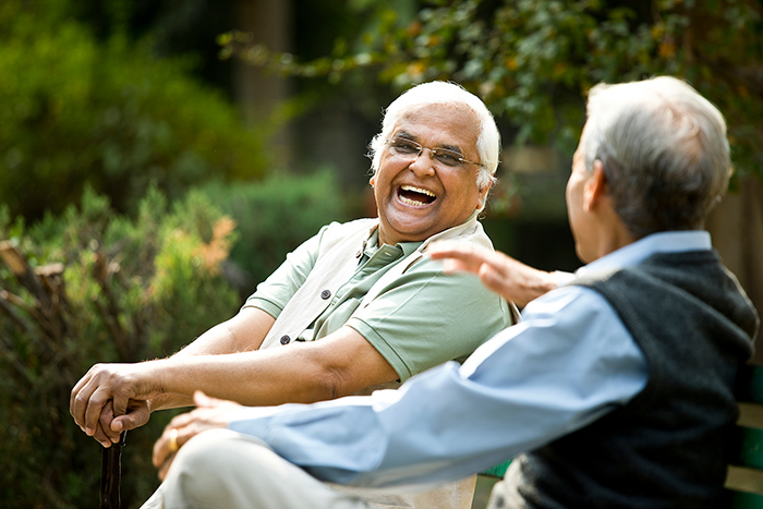 Two senior men sitting at park bench outside laughing