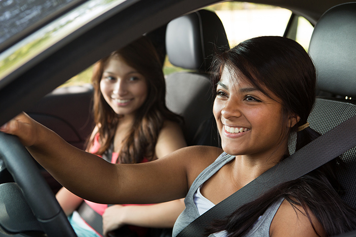 Two smiling teenage girls in front seat of car with one driving