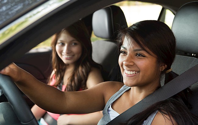 Two smiling teenage girls in front seat of car with one driving