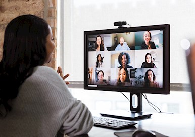 Woman sitting at desk looking at computer monitor talking to others on virtual meeting