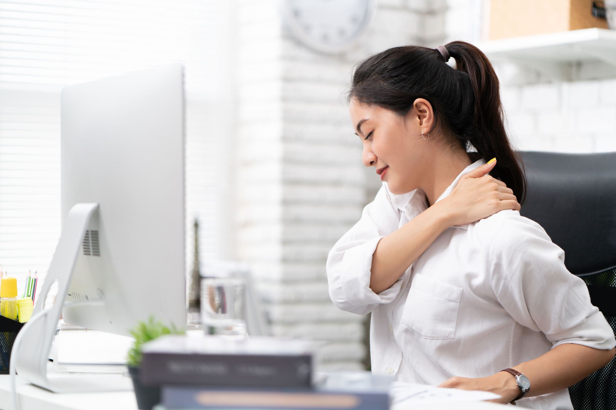 Woman sitting at desk holding her shoulder