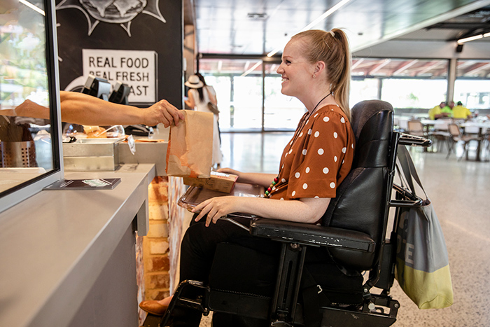 Woman in motorized wheelchair being handed brown bag of food at counter