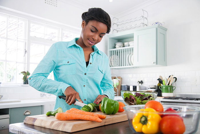 Woman in kitchen cutting fresh vegetables with knife